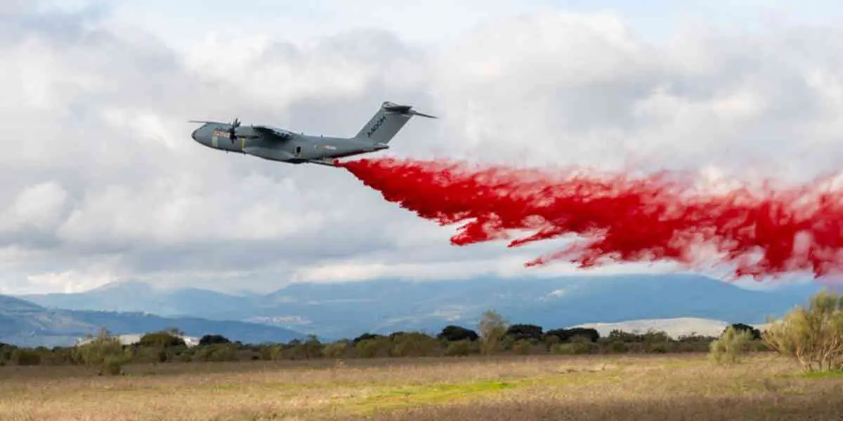 A400M-incendie - Votre Actualité au Quotidien Plane releasing a red smoke trail over an open field with mountains in the distance.